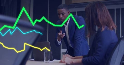 Colleague pointing at laptop presenting analytics with colorful line charts in boardroom