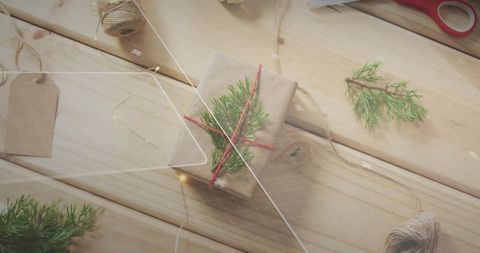 Kraft gift wrapping with red twine and evergreen sprig on rustic wood tabletop