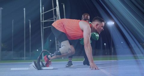 Paralympic sprinter preparing for race with coach at night stadium