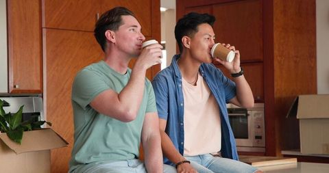Diverse gay couple enjoying coffee together in modern kitchen