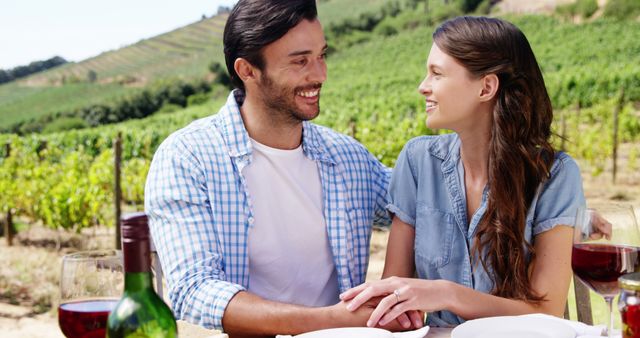 A young Caucasian couple enjoys a romantic wine tasting date in a vineyard, with copy space. Their affectionate gaze and smiles suggest a moment of connection and leisure.