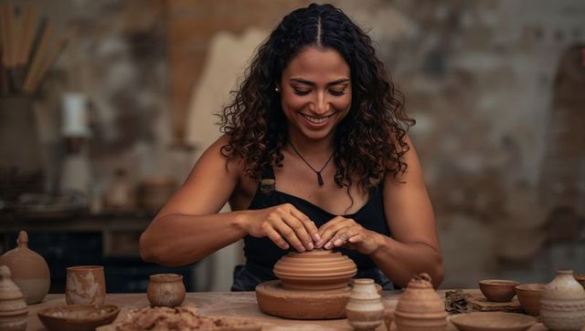 Smiling artisan centering clay and shaping pot on banding wheel in rustic ceramics studio