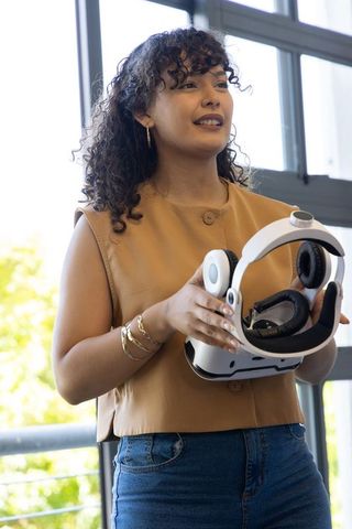 Young woman holding white vr headset presenting virtual reality demo in modern workspace