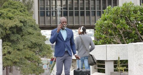 Executive walking and talking on phone while pulling suitcase on urban pedestrian walkway