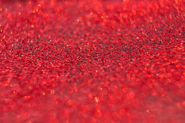 This image captures a close-up view of red glitter, creating a sparkling and festive background. Ideal for use in holiday-themed designs, Christmas cards, party invitations, and festive decorations. The vibrant red and shimmering effect make it perfect for adding a touch of celebration and joy to any project.