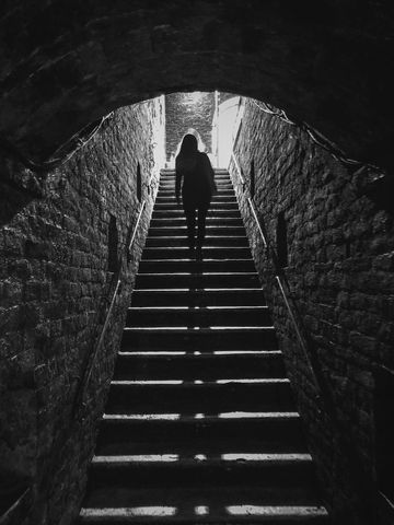 Silhouette of Person Ascending Dimly Lit Stone Staircase