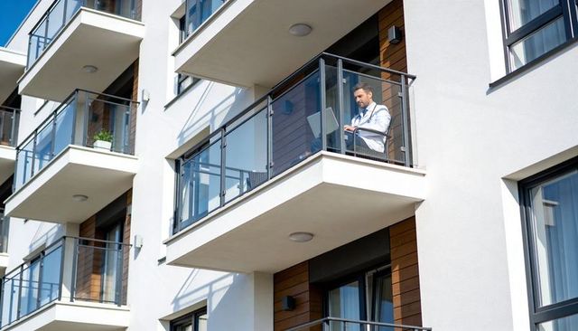 Professional working on laptop on glass-railed balcony of modern apartment building