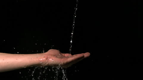 Human Hand in Slow Motion With Water Flowing Against Dark Background