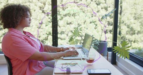 Remote worker typing on laptop at bright window desk with plants and digital network overlay