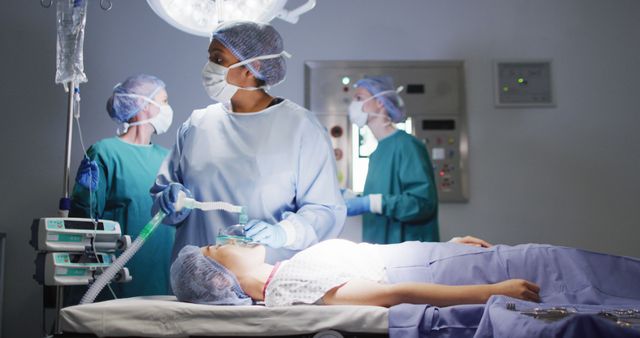 Image of biracial female surgical assistant giving gas to asian female patient in operating theatre. Hospital, medical and healthcare services.