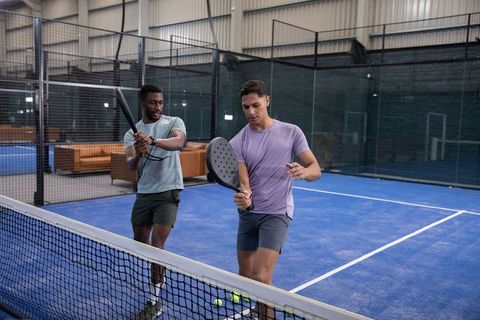 Two men practicing padel near net on indoor blue court, coaching teamwork and technique