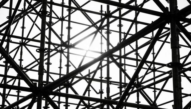 Backlit industrial scaffolding lattice creating geometric steel pattern with sun glare