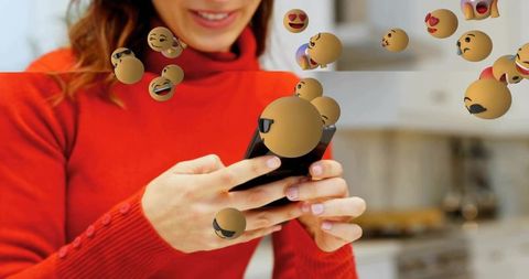 Woman in red turtleneck texting on smartphone with floating emoji bubbles in cozy kitchen