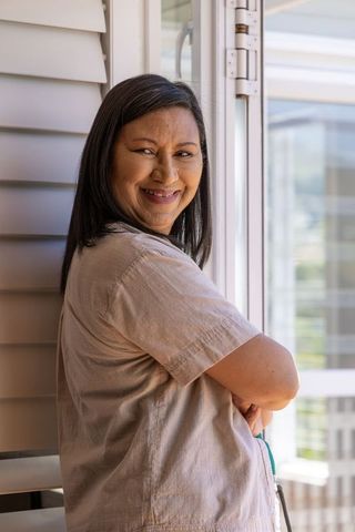 Asian mature woman smiling and leaning with arms crossed by sliding glass door