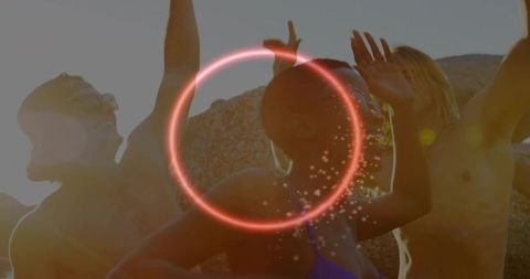 Friends celebrating on rocky beach with neon ring, golden hour backlight and lens flare
