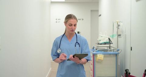 Female Clinician Walking Hospital Corridor Consulting Tablet in Modern Bright Facility