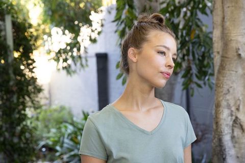 Thoughtful young woman standing in garden by tree wearing green v-neck tee looking right