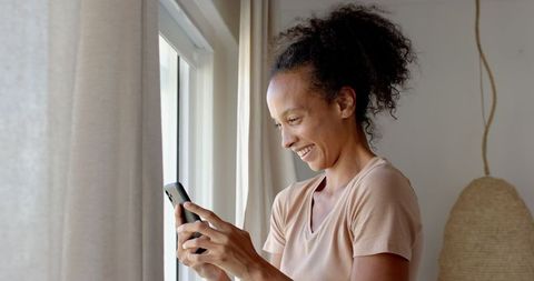 Smiling Woman Enjoying Smartphone at Sunny Window