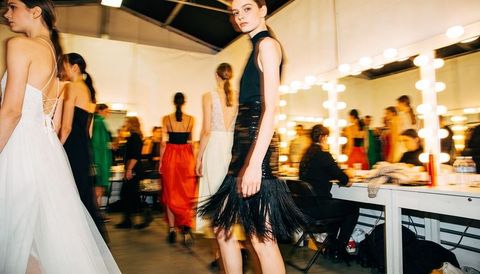 Backstage fashion models preparing for runway show near illuminated vanity mirrors