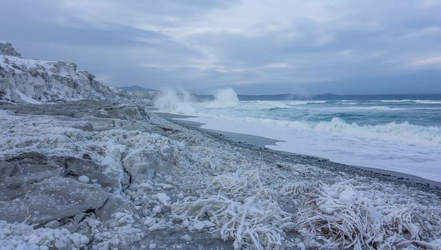 Icy rocky coastline with ice-coated seaweed and crashing waves on winter shore