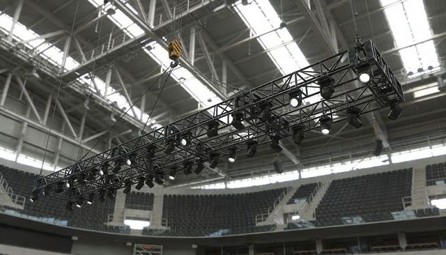 Overhead lighting truss suspending from crane across indoor arena bowl with rigging