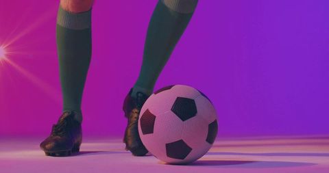 Soccer player controlling ball with black cleats and green socks in neon pink purple studio