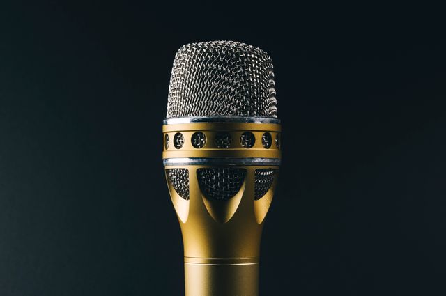 This image captures a close-up view of a gold and silver microphone against a black background. It can be used for music or sound recording related articles, concert promotions, podcasts, studio advertisements, and audio equipment websites.