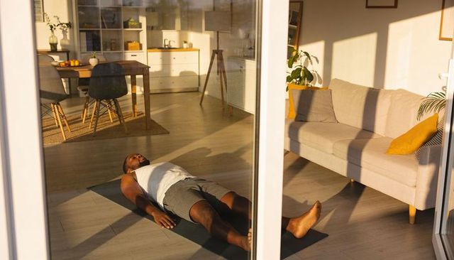 Man practicing restorative yoga in sunlit minimalist living room for home wellness