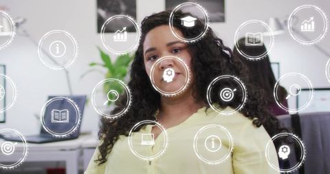 Curly professional wearing pale yellow blouse seated in modern office with digital icons
