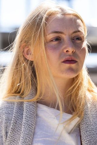 Young blonde woman gazing upward, freckled face backlit by waterfront sunlight