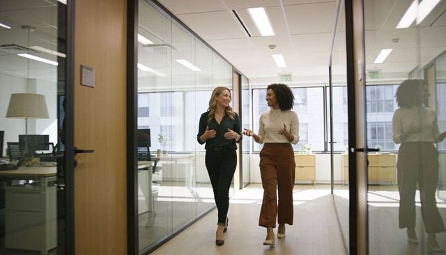 Two coworkers walking and talking in modern glass office corridor, teamwork and collaboration