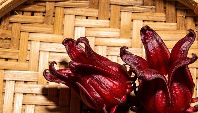 Close-up roselle calyces on woven bamboo tray glossy crimson lobes and veined texture