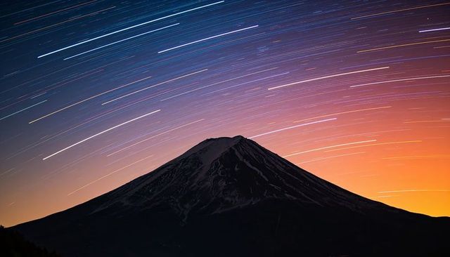 Majestic conical volcano silhouette with colorful star trails over twilight horizon