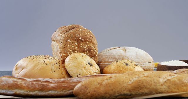 A diverse assortment of breads placed on wooden table. Includes whole grain loaf, white bread, baguette, and round loaves. Ideal for showcasing bakery products, bread recipes, or healthy food choices. Perfect for use in bakery promotions, cookbooks, and food-related marketing materials.