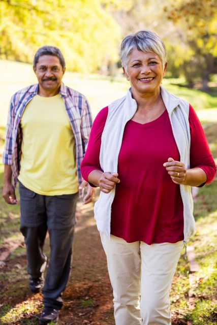 Mature couple enjoying a walk in a park, showcasing happiness and active lifestyle. Ideal for use in health and wellness promotions, senior living advertisements, and articles about healthy aging and outdoor activities.