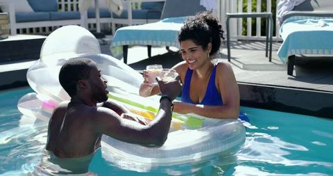 Diverse couple toasting on clear inflatable in sunny backyard pool