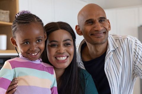 Happy african american family smiling together in modern kitchen, parents embracing daughter