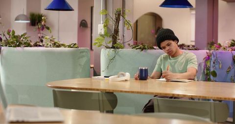 Young man writing in coworking lounge with pastel mint booths and plants