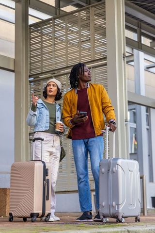 Diverse travelers standing under transit canopy pointing ahead, holding luggage and coffee