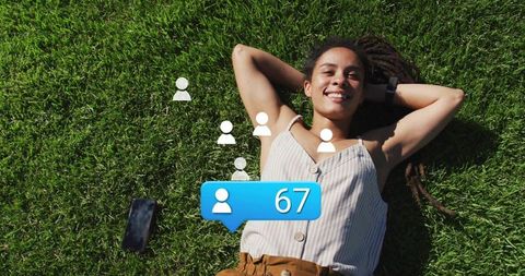 Smiling woman lying on grass relaxing with smartphone and social followers notification 67
