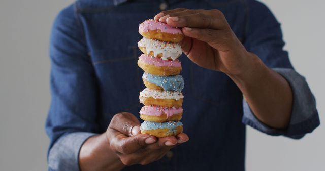 Close-up shot shows person holding a stack of colorful glazed donuts with sprinkles. Perfect for use in food blogs, dessert recipes, advertisements for bakeries, and promotions for sweet treats. Highlights emphasis on presentation and gourmet pastries.