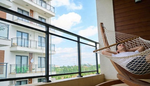 Young man relaxing in hammock on modern apartment balcony with sunny green view
