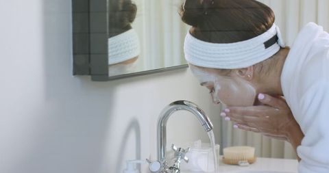 Woman practicing skincare routine washing face in bright bathroom