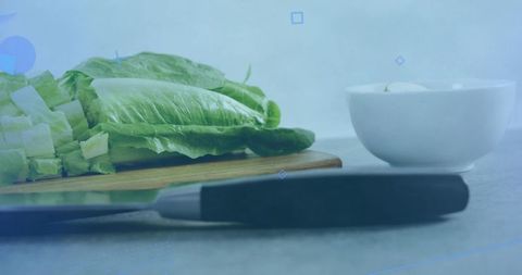 Chopping romaine on wooden board with black-handle knife and white bowl for salad prep