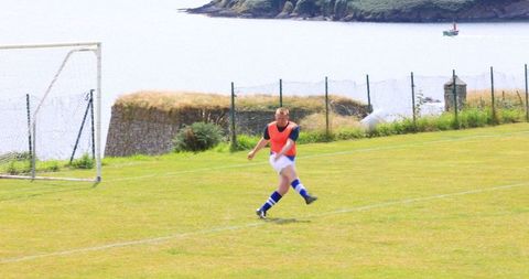 Soccer player kicking on grassy field by riverside scenery