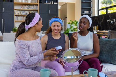 Friends having at-home skincare night sharing cream, mirror and relaxing together