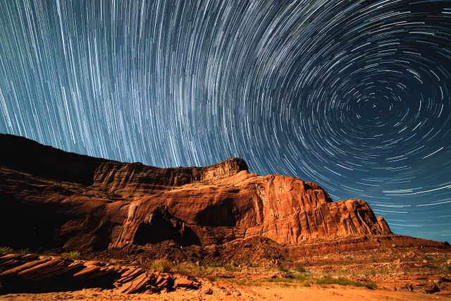 Stunning time-lapse display of star trails over dramatic red rock formations in a remote desert. Ideal for nature enthusiasts, astronomy content, science presentations, travel brochures, or as an eye-catching digital wallpaper. Captures the beauty of the natural night sky and geological splendor.