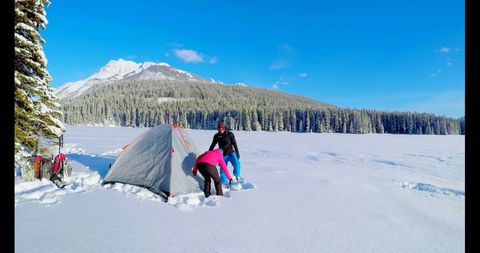 Couple setting up tent in snowy mountain landscape