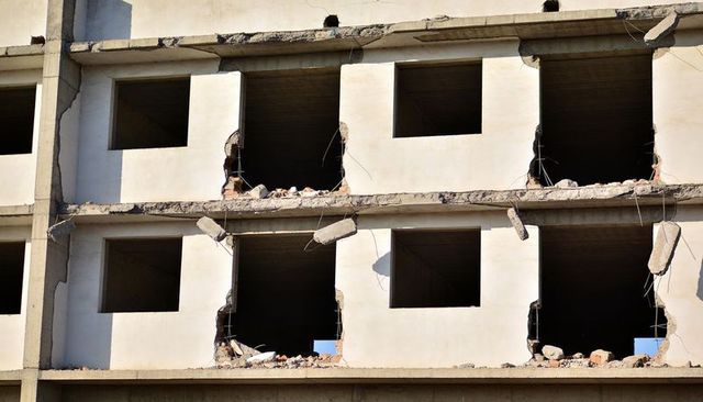 Cracked concrete facade with hanging debris and exposed rebar on demolished building