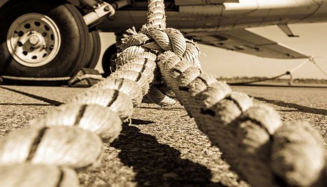 Closeup braided tie-down ropes securing light aircraft landing gear on sunlit tarmac